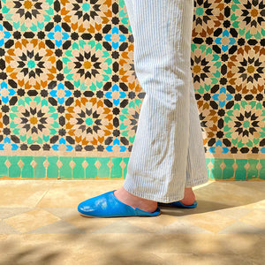 Femme portant des babouches marocaines en cuir bleu devant un mur en zellige