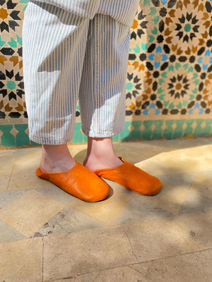Babouches marocaines en cuir orange faites main, portées dans un riad au sol en pierre