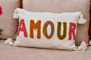 Coussin AMOUR en coton écru brodé au punch needle, lettres roses, ocre et kaki, pompons blancs