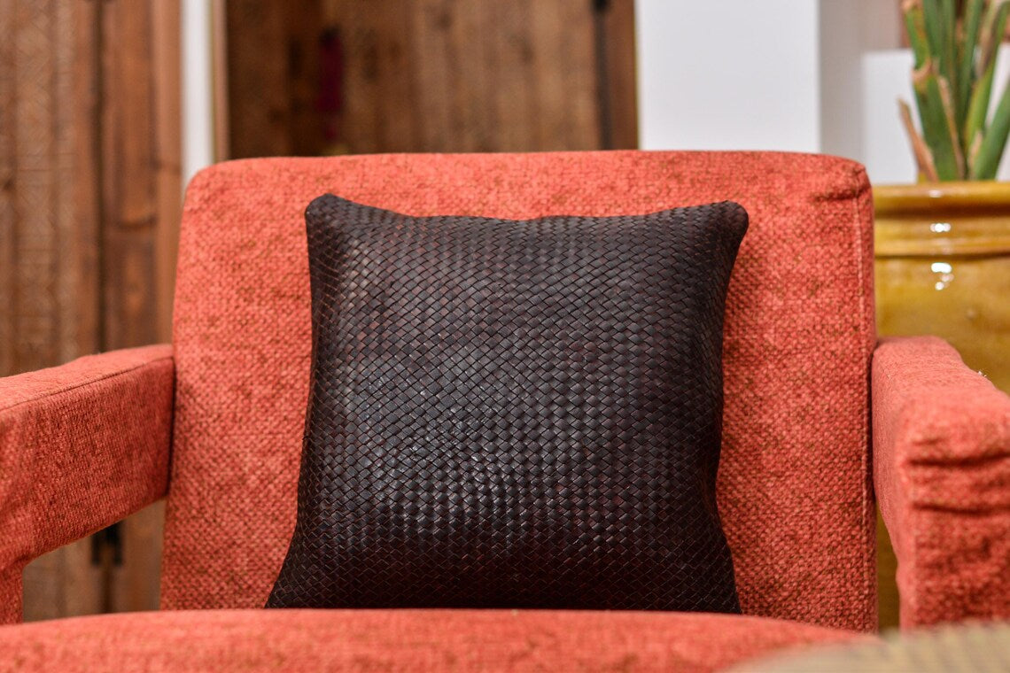 Coussin carré en cuir tressé marron foncé posé sur un fauteuil terracotta, vue de face