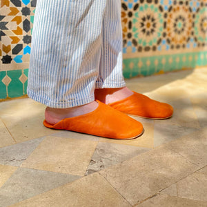 Femme portant des babouches marocaines en cuir orange devant un mur en zellige