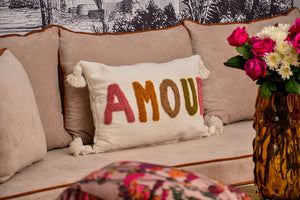Coussin décoratif AMOUR brodé main, lettres multicolores en laine, posé sur un canapé beige