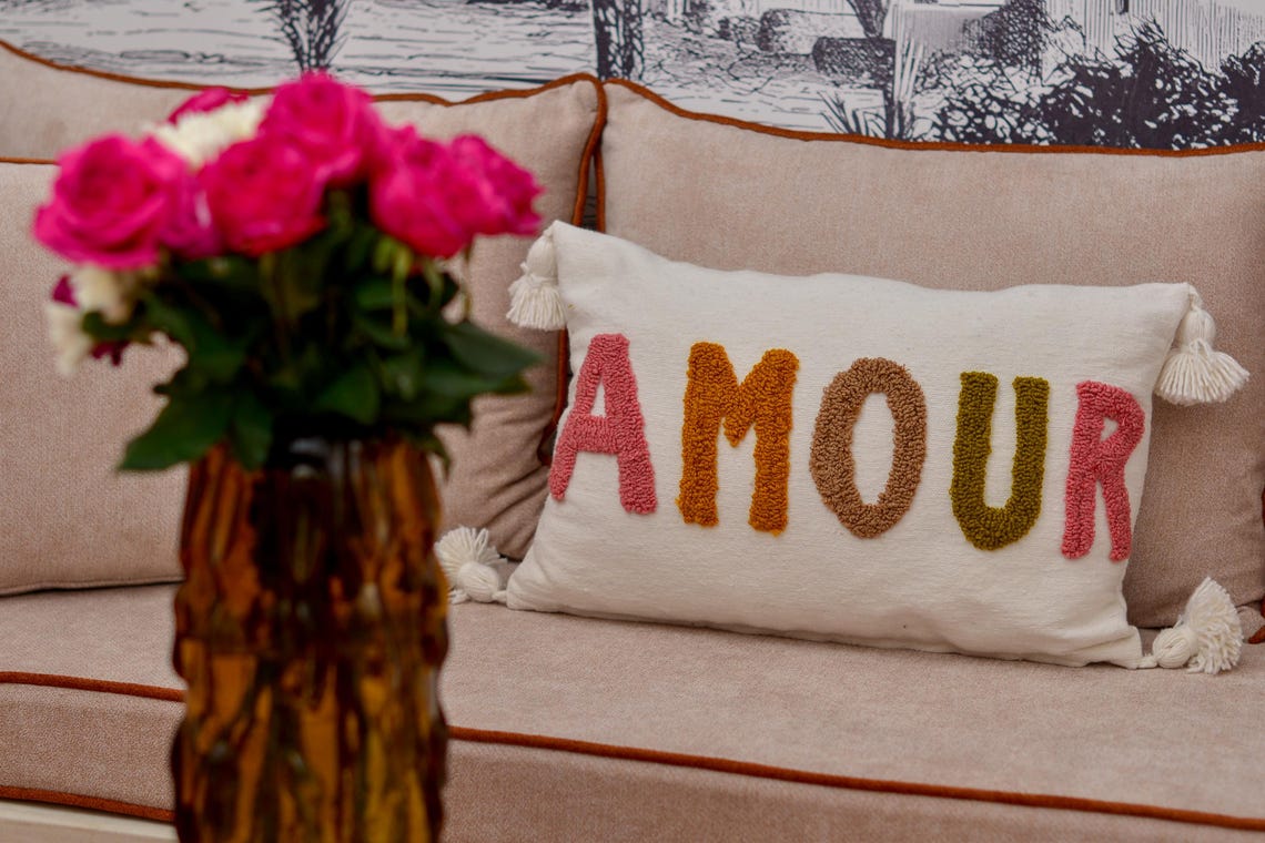 Coussin AMOUR fait main sur banquette de salon marocain, vase ambré et bouquet de roses