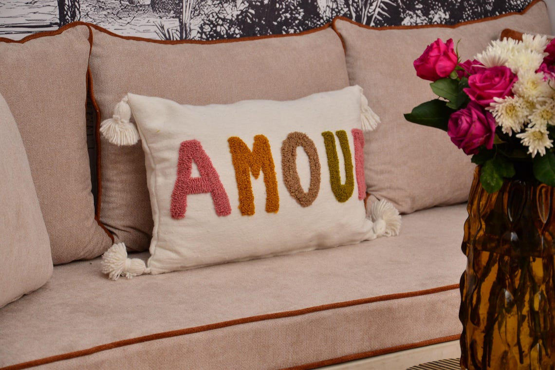 Coussin AMOUR posé sur un canapé, ambiance salon bohème chic avec papier peint toile de Jouy