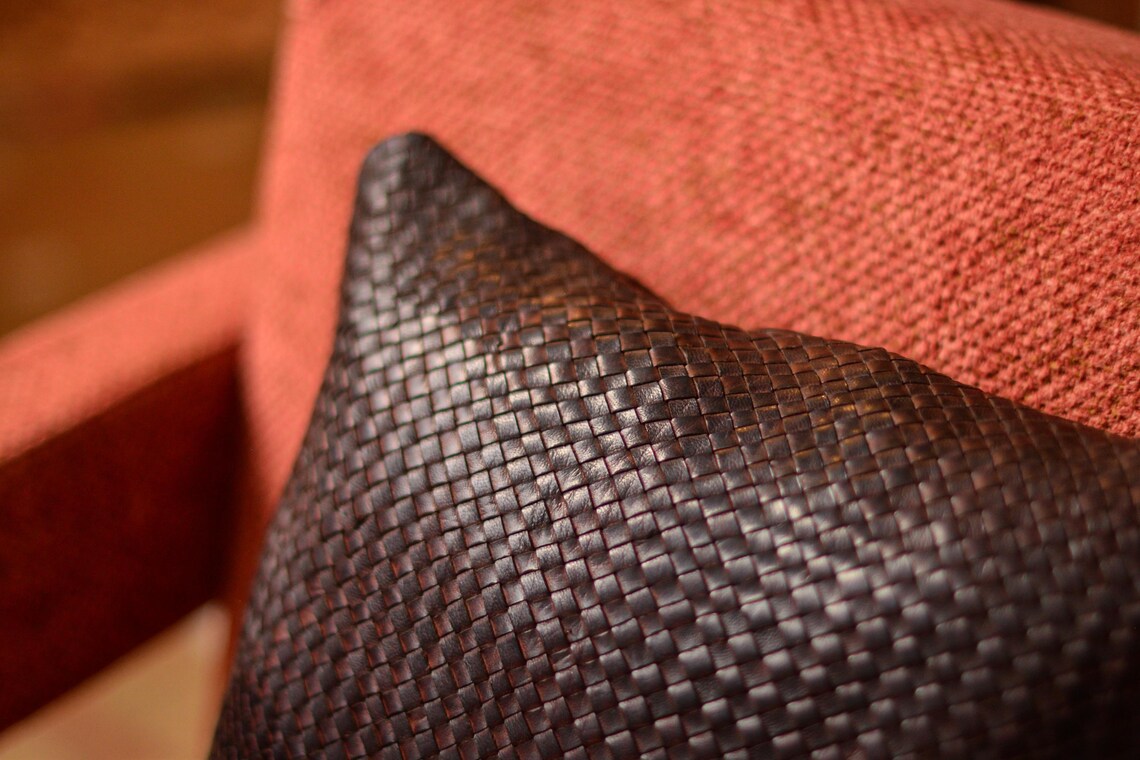 Coussin carré en cuir tressé à la main, teinte marron chocolat, sur fauteuil en tissu orange