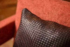 Coussin carré en cuir tressé à la main, teinte marron chocolat, sur fauteuil en tissu orange