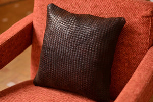 Coussin en cuir tressé marron sur fauteuil, ambiance salon marocain avec plante et poterie